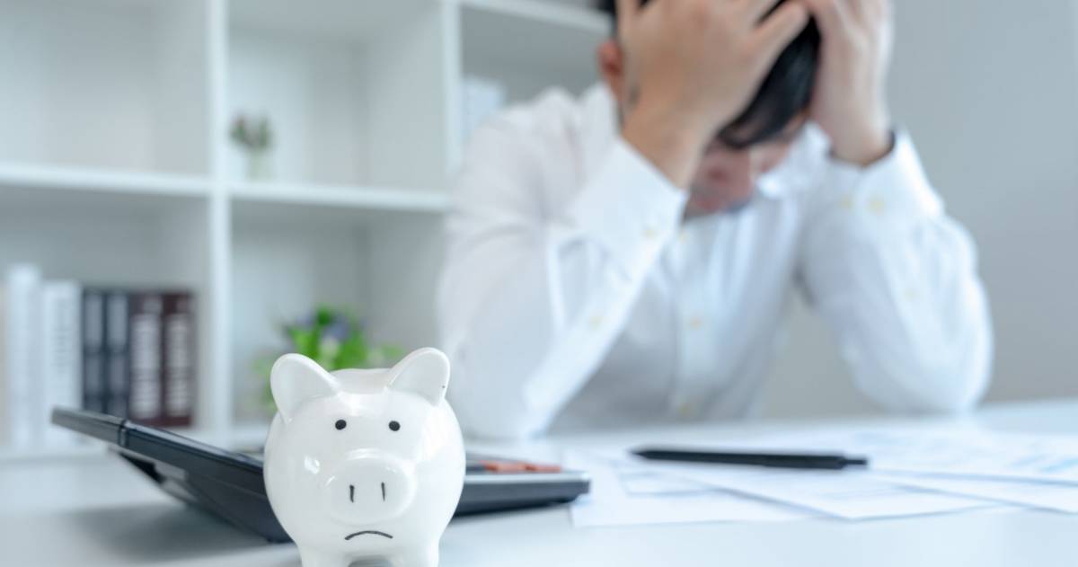 Gestreste zakenman zit achter zijn bureau en kijkt naar rekeningen en houdt zijn handen op zijn hoofd