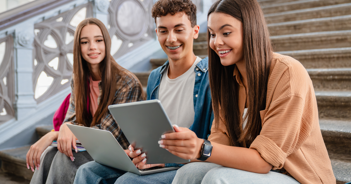 Scholieren zitten bij elkaar op een trap en bekijken een leuk bericht op laptop