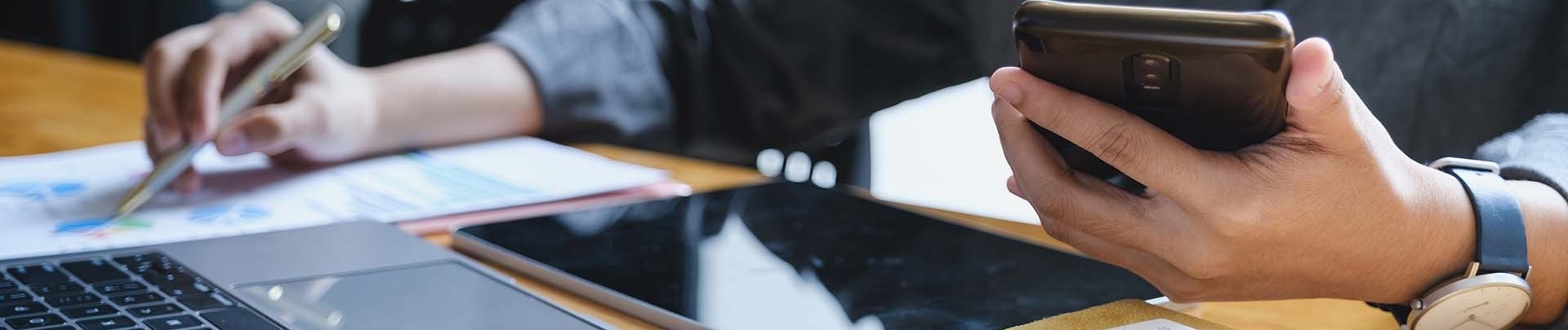 Vrouw met een pen en een telefoon in haar hand berekent financiële zaken achter een latop 